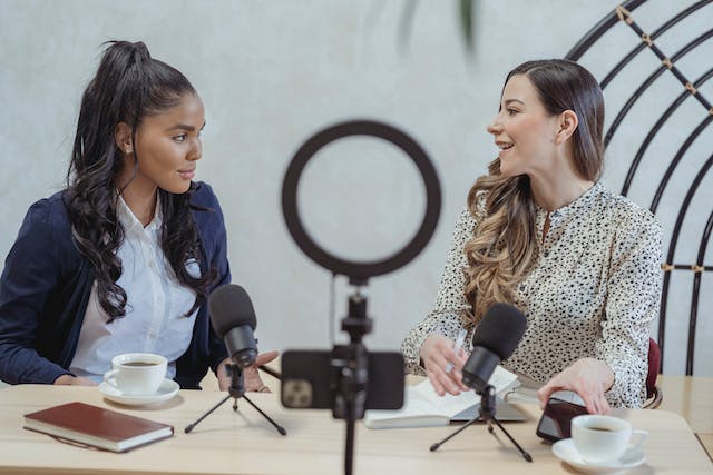 Zwei Frauen nehmen gemeinsam einen Business-Podcast auf und trinen dabei einen Kaffee.