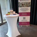 Bild vom Messestand mit Rollup und Stehtisch mit Werbemitteln.
