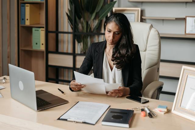 Eine Unternehmerin sortiert an ihrem Schreibtisch Unterlagen. Neben ihr steht ein Laptop für den Online-Austausch mit Gleichgesinnten.
